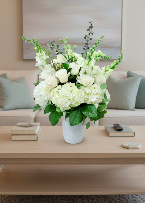 Bouquet of white flowers with green leaves in a white vase on a light background