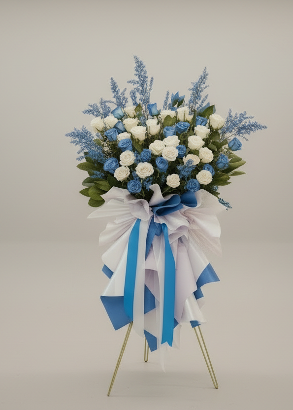 Floral arrangement on a stand with blue and white ribbons against a plain background