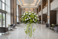Bouquet of green and white flowers with ribbons on a stand against a plain background