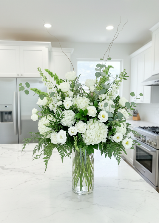Bouquet of white flowers in a clear vase on a wooden table with a blurred indoor background