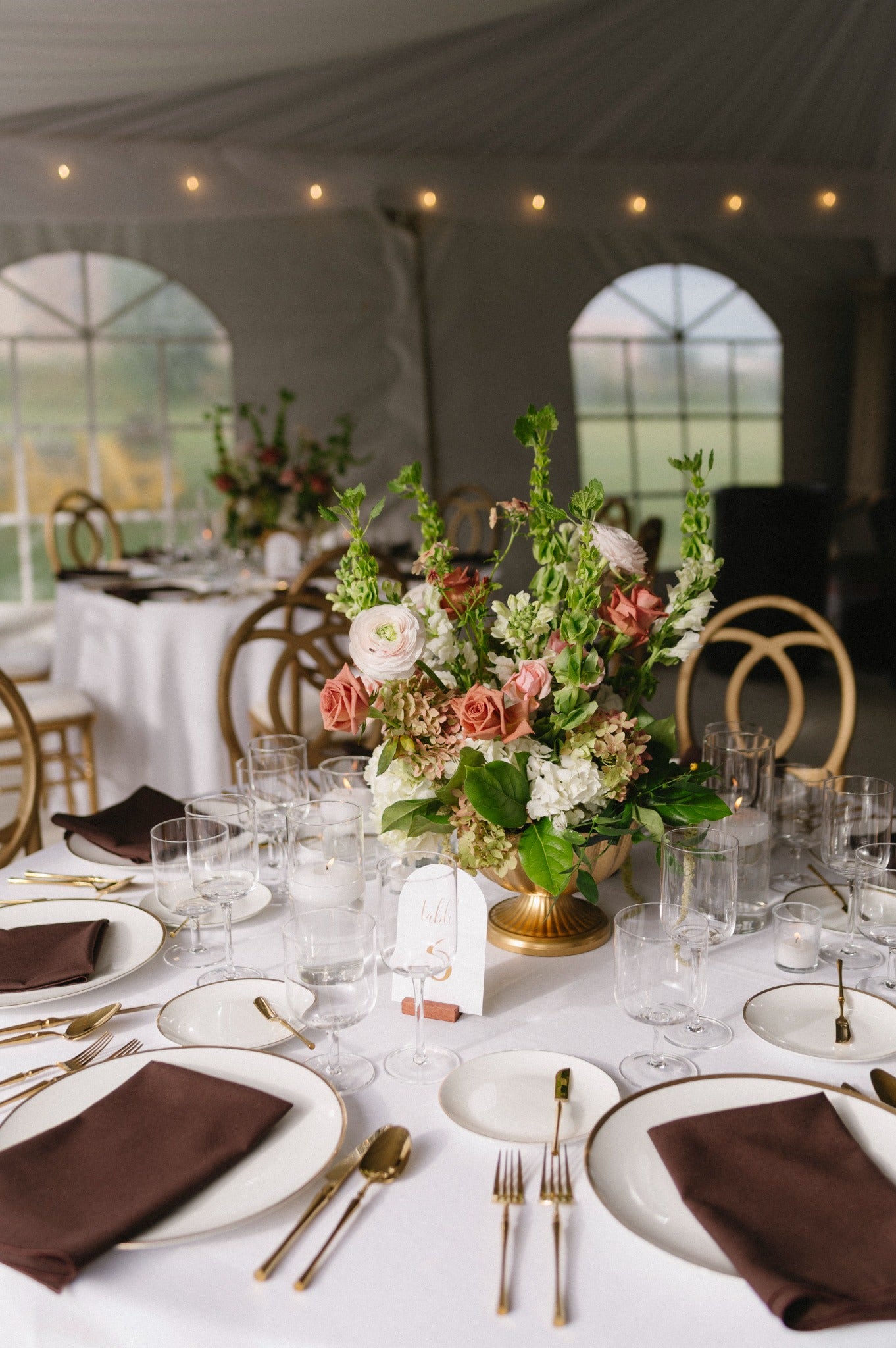 Low reception centrepiece in a gold vessel with dusty rose roses, blush ranunculus, hydrangeas and fresh green stems