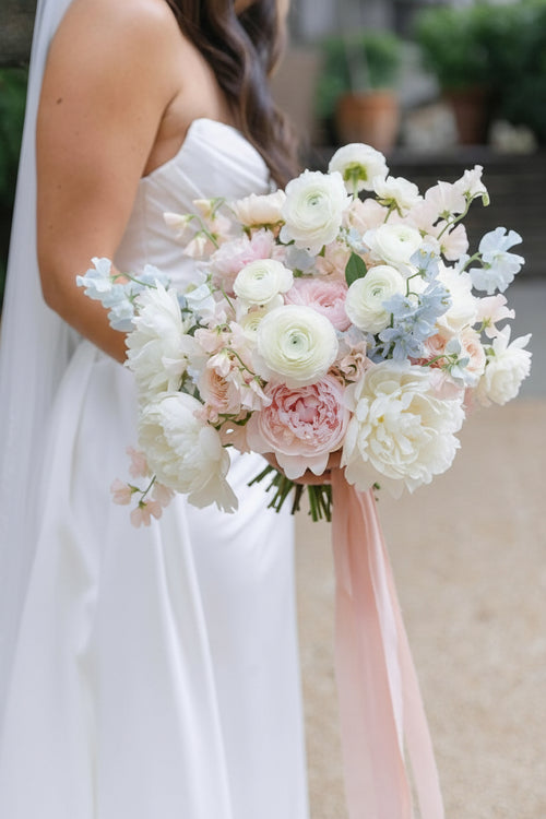 Bride holding a bouquet of pink, orange, and red flowers with a blurred background.